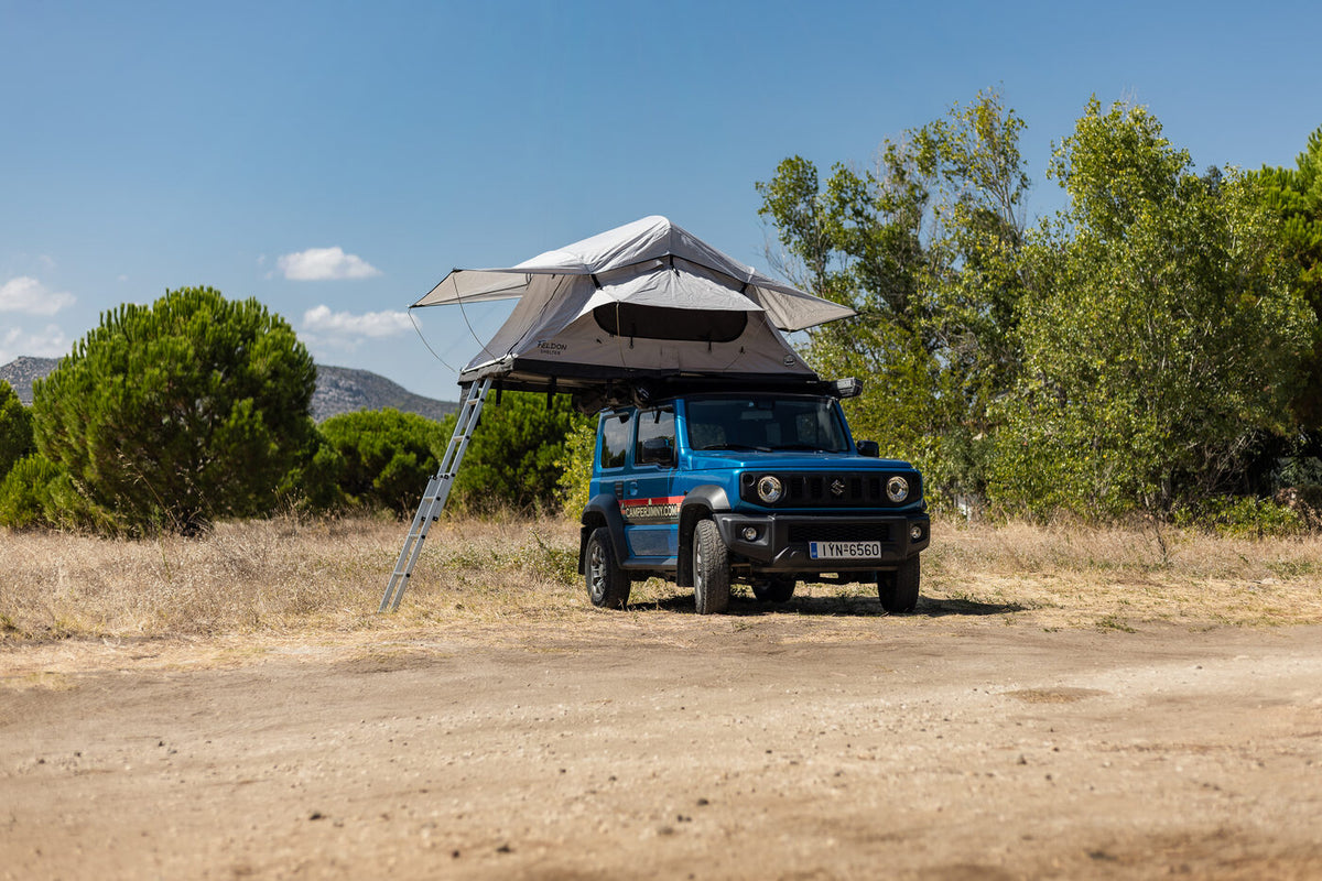 Blue Suzuki Jimny with the Feldon Shelter Crow's Nest roof top tent open at a forest camp