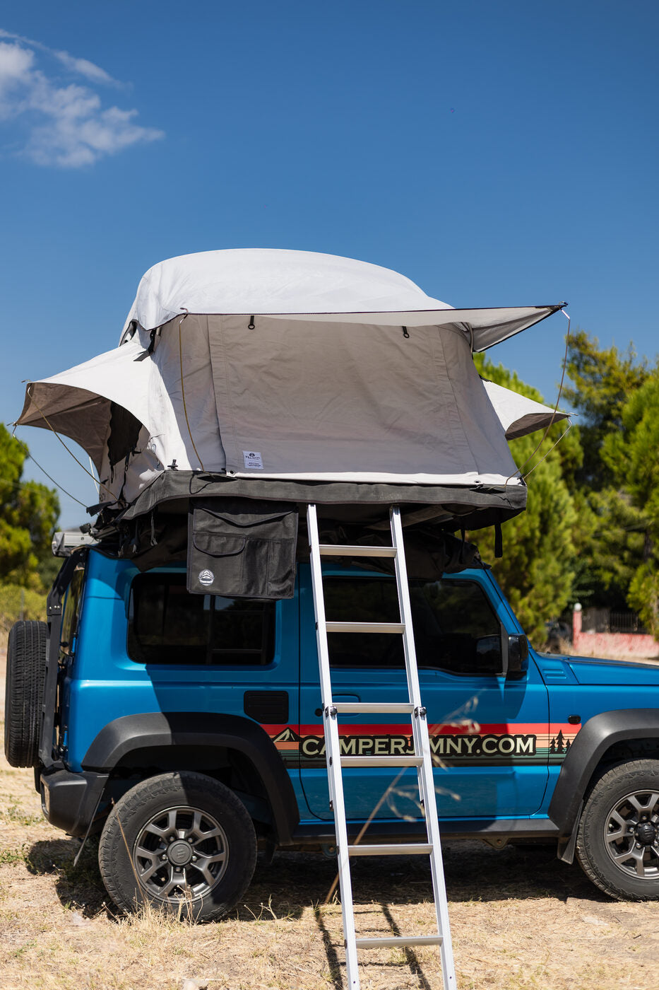 Blue Suzuki Jimny from the side with its roof top tent open and the ladder down