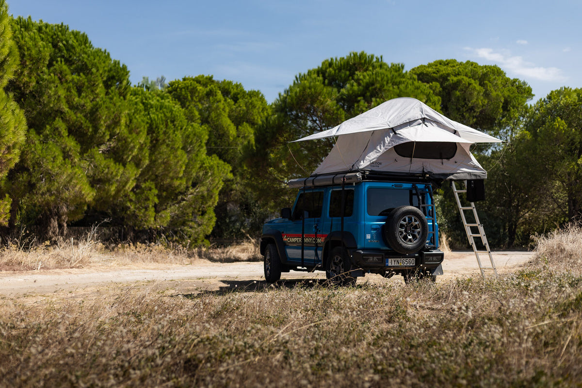 Blue Suzuki Jimny seen from behind with the roof top tent open and the ladder in place
