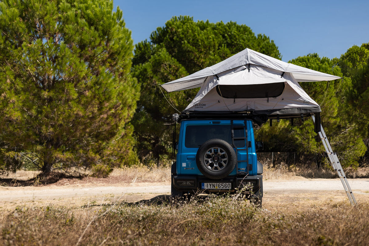 Rear view of the blue Suzuki Jimny with the roof top tent pitched between pine trees