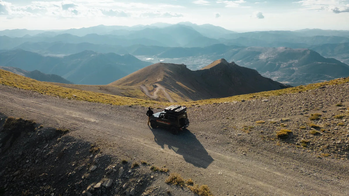 Drone view of the green CamperJimny on a high mountain road with wide views across Greece