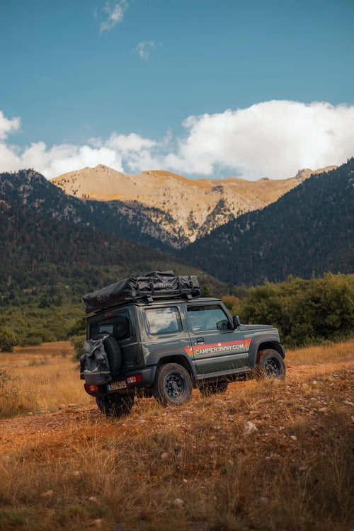Green Suzuki Jimny with a roof top tent in front of rocky mountain peaks on a road trip in Greece