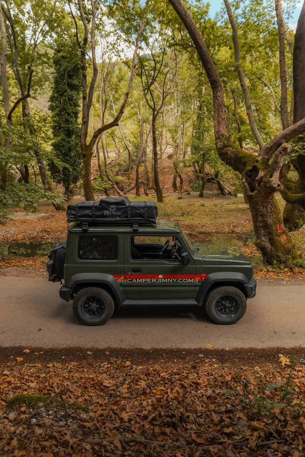 Side view of the green CamperJimny 4x4 rental with the roof top tent closed on a tree-lined road