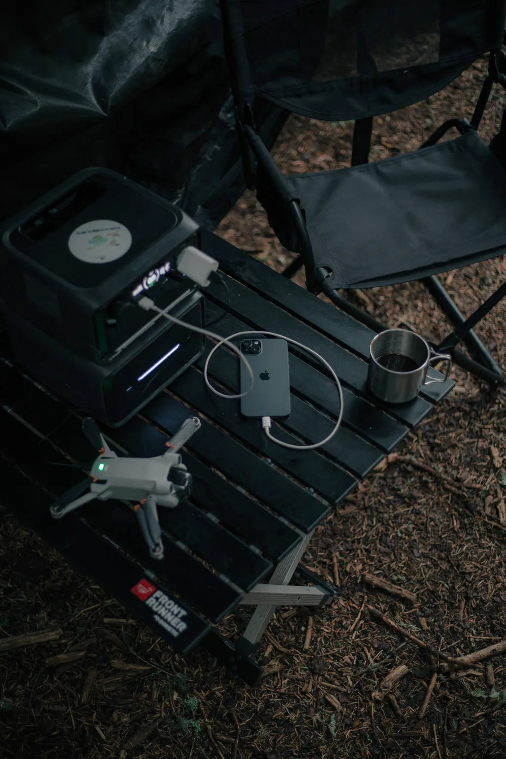 Portable power station charging a phone on the camp table next to the Jimny Green Crow's Nest